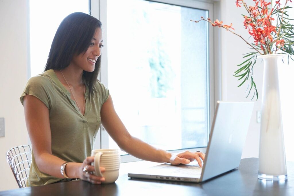 Woman with a Mug in Her Hand, Smiling at Computer | Online Therapy: Telehealth | Rooted Counseling and Wellness | Best Counseling in Draper Utah | Rooted Therapy and Wellness