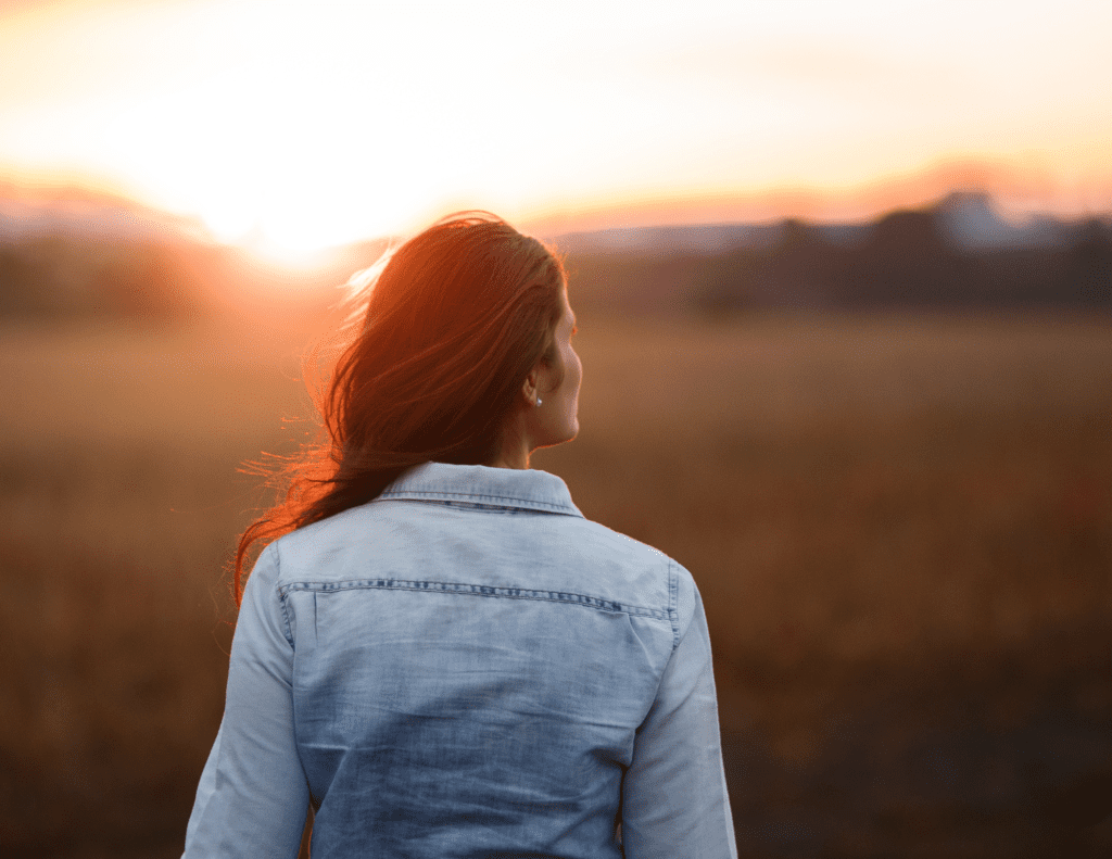 Woman Standing in a Field, Looking at Sunset | Holistic Trauma Healing Program | Rooted Counseling & Wellness | Holistic Trauma Healing | Holistic Trauma Recovery